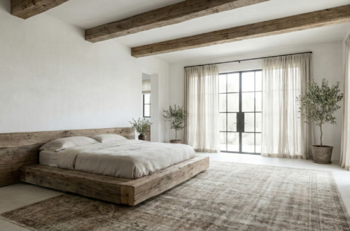 A wide-angle view of a serene sanctuary showcasing modern rustic bedroom ideas, featuring a low reclaimed oak platform bed, exposed ceiling beams, white lime-washed walls, and large steel-framed windows draping soft natural light onto a vintage wool rug.